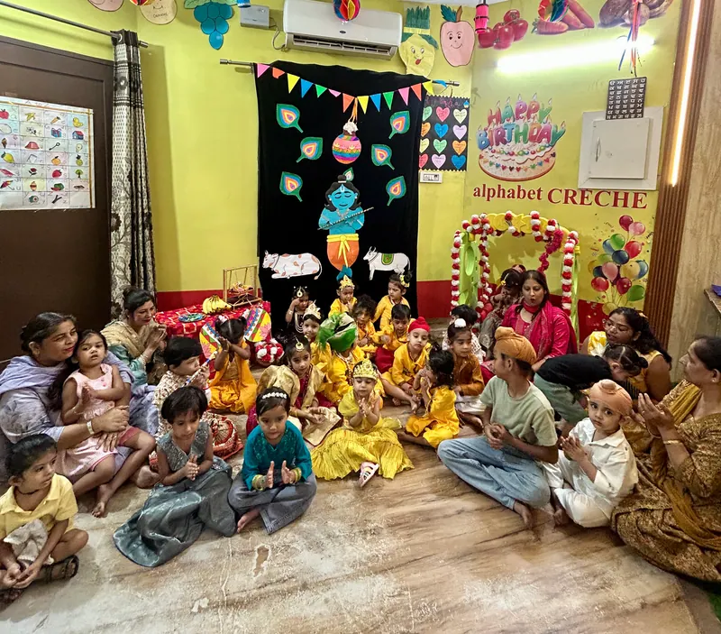 Children dressed for Janmashtami sitting together beneath the alphabet CRÈCHE banner
