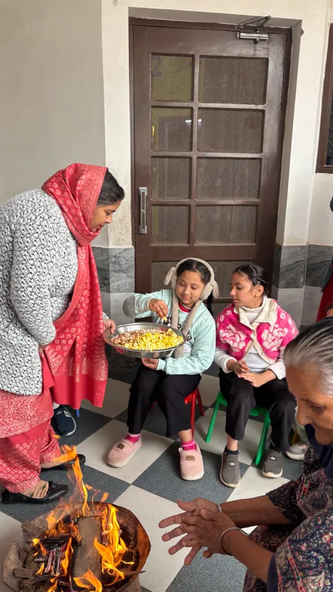 Children around a small Lohri bonfire with a teacher holding a plate of popcorn